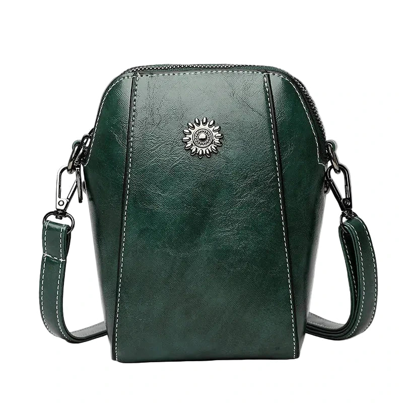 Green leather crossbody bag with a decorative emblem on a white background