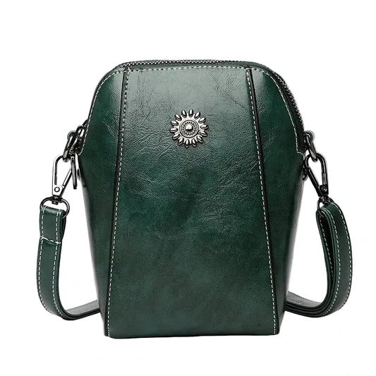 Green leather crossbody bag with a decorative emblem on a white background