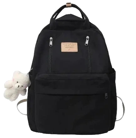 Black backpack with a small teddy bear attached on a gray background