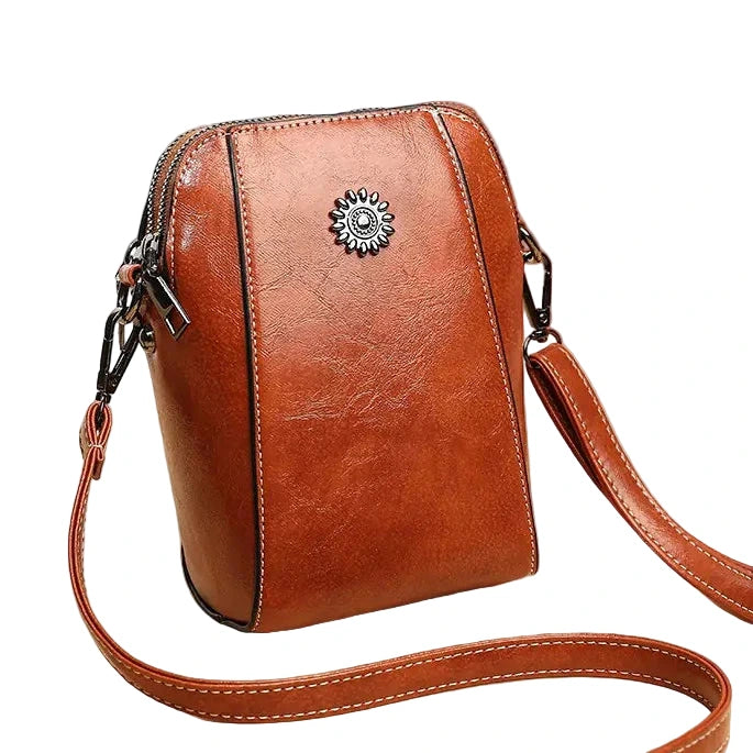 Brown leather crossbody bag with decorative emblem on a white background