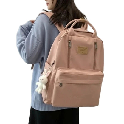 Person wearing a beige backpack with a teddy bear charm.