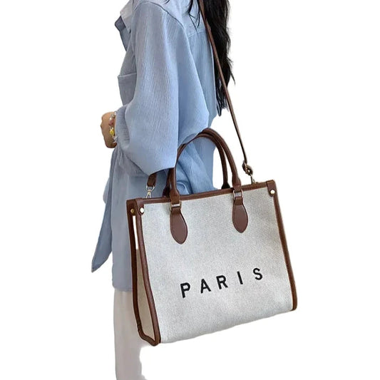 Person holding a tote bag with 'PARIS' text against a white background