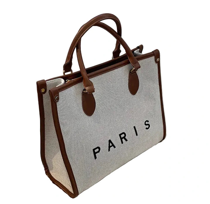 Gray tote bag with brown handles and trim, featuring the word 'PARIS', on a white background