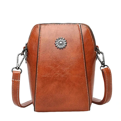 Brown leather crossbody bag with a decorative emblem on a white background