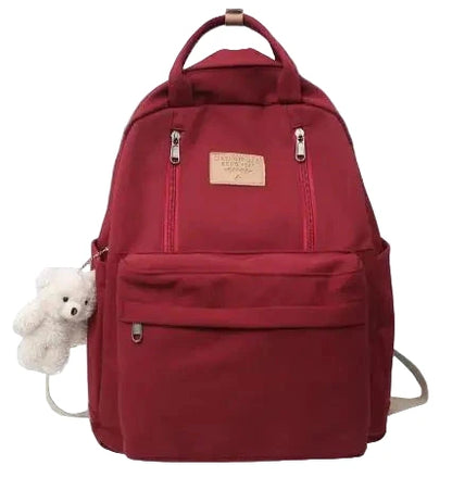 Red backpack with a teddy bear peeking out from a pocket on a gray background